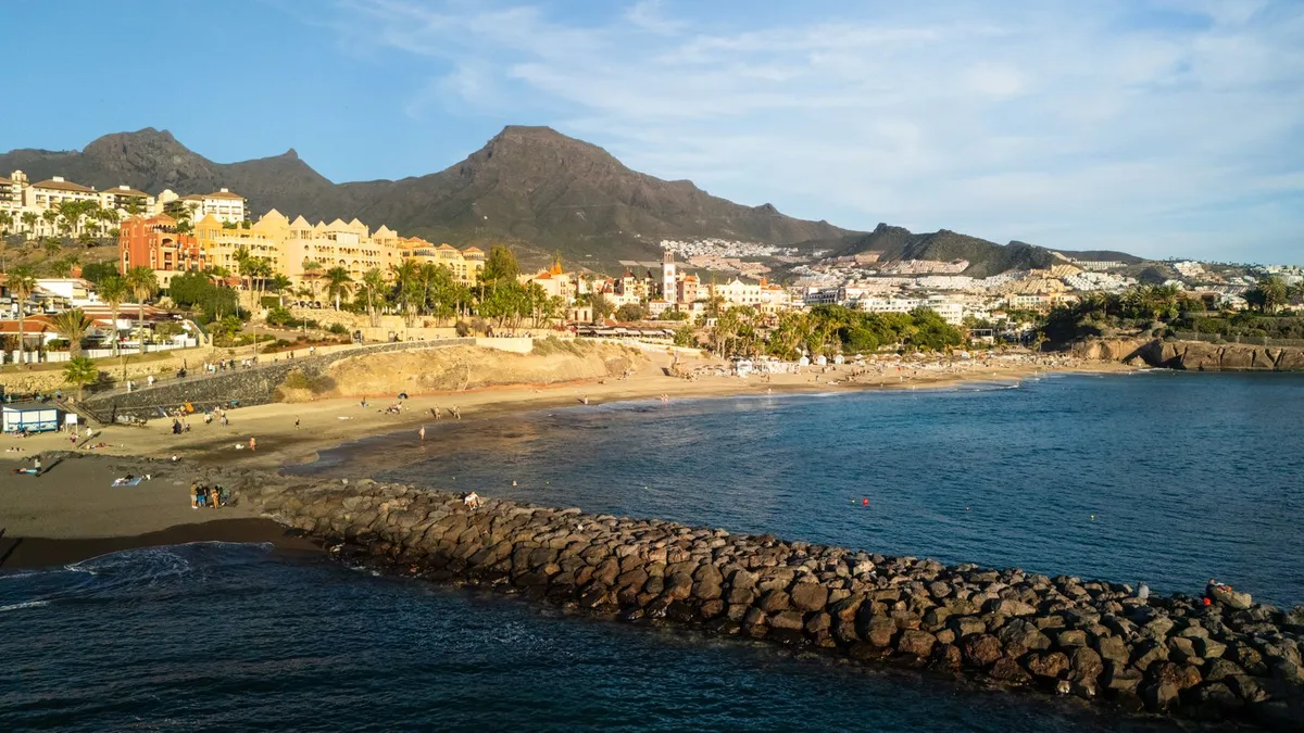 Aerial view of Costa Adeje's cove beach and resorts at sunset, with the mountains behind.