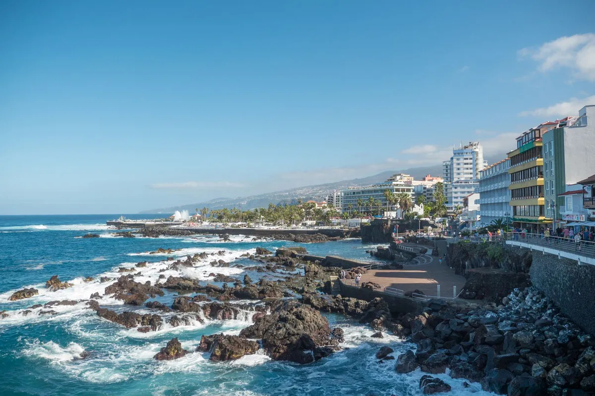 The lava-rock coast and colourful seafront of Puerto de la Cruz, backed by green northern mountains.