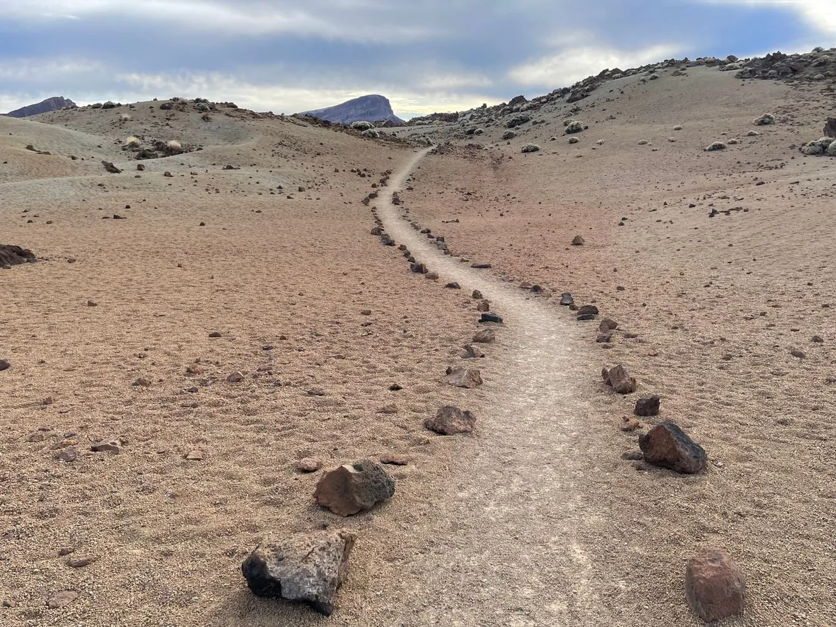 A rocky-marked footpath crossing the arid volcanic plateau of Teide National Park toward a distant peak